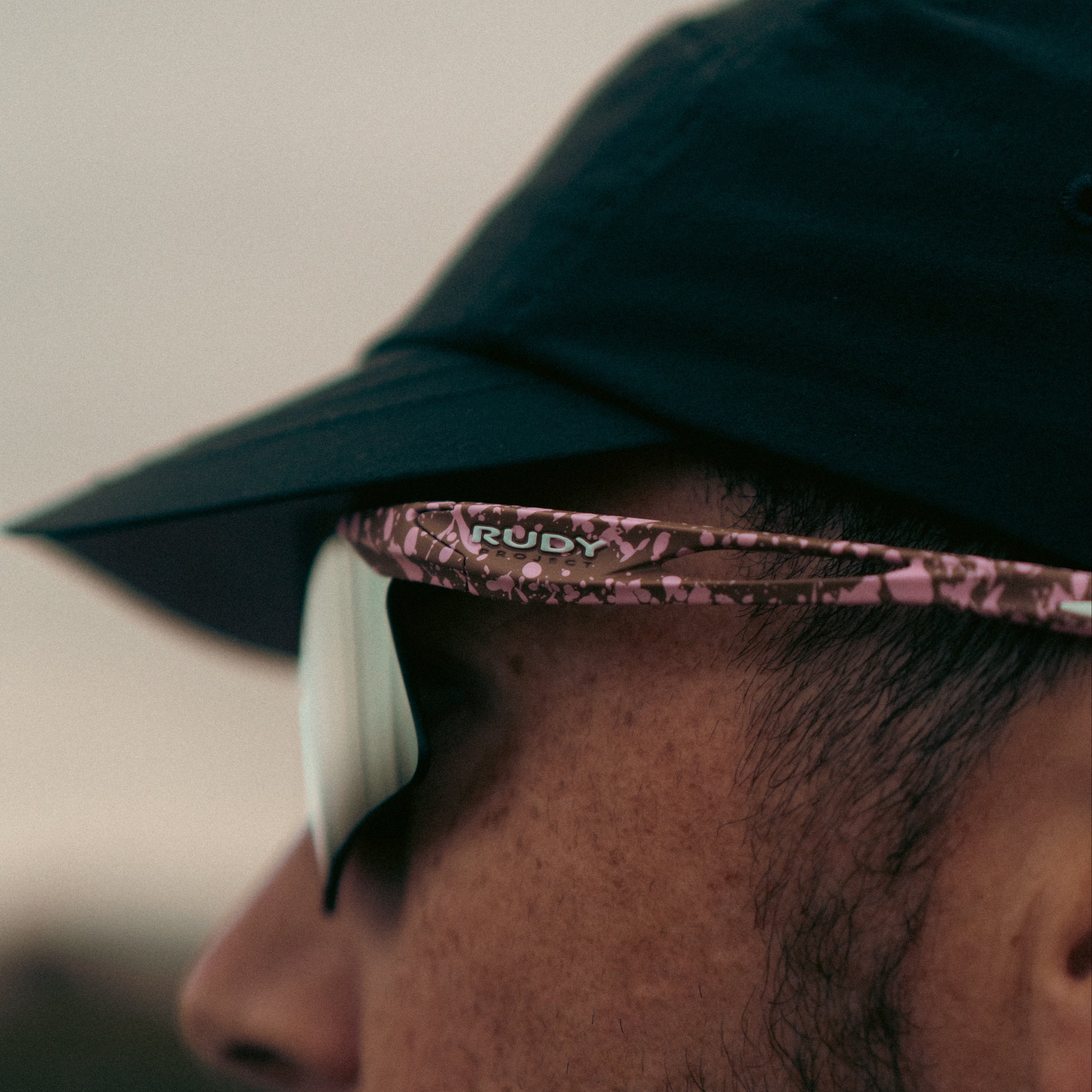 Close-up of a person wearing a green cap and sunglasses with a blurred background